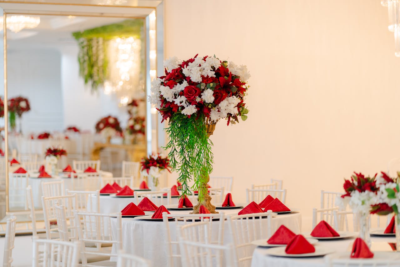 Bright wedding venue setup featuring elegant floral centerpieces and red napkins on tables.